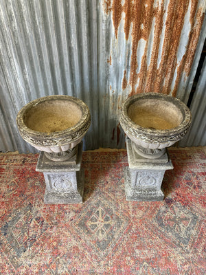 A pair of large cast stone classical urns on pedestals