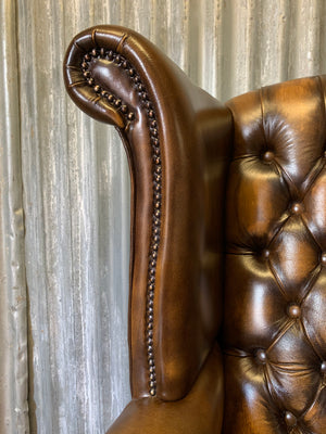 A brown wingback Chesterfield armchair with button back