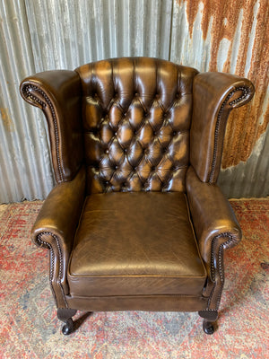 A brown wingback Chesterfield armchair with button back
