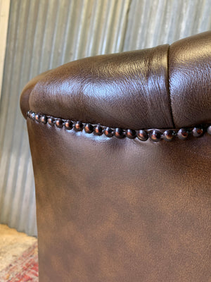 A brown wingback Chesterfield armchair with button back