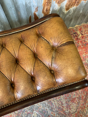 A buttoned tan leather footstool
