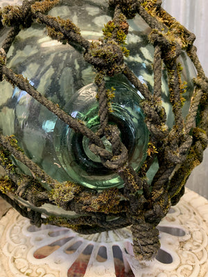 A large glass float in its original rope cage