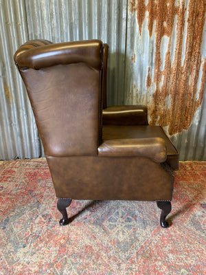 A brown wingback Chesterfield armchair with button back
