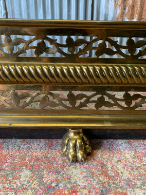 A large Victorian brass fender with lion paw feet