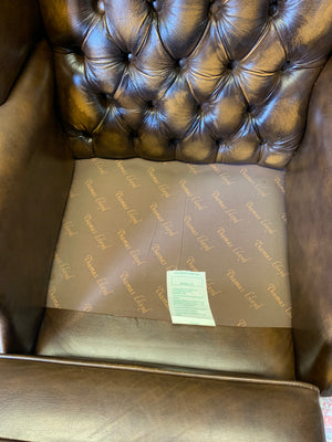 A brown wingback Chesterfield armchair with button back