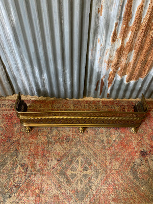 A large Victorian brass fender with lion paw feet