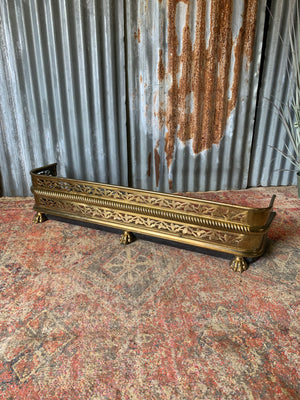 A large Victorian brass fender with lion paw feet