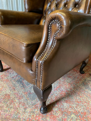 A brown wingback Chesterfield armchair with button back