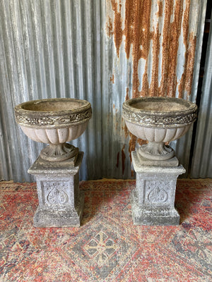 A pair of large cast stone classical urns on pedestals