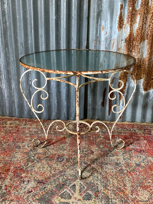 A French-style iron garden table with glass top