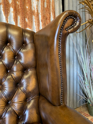 A brown wingback Chesterfield armchair with button back