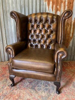A brown wingback Chesterfield armchair with button back