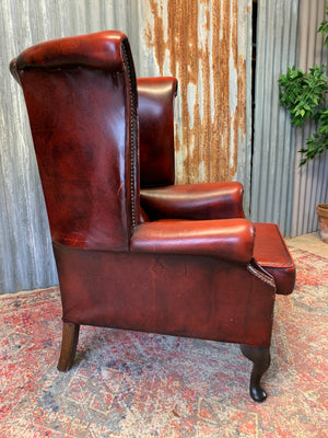 An oxblood wingback Queen Anne-style armchair