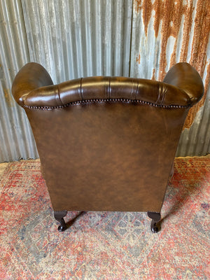 A brown wingback Chesterfield armchair with button back