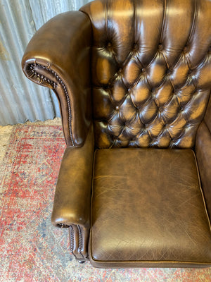 A brown wingback Chesterfield armchair with button back