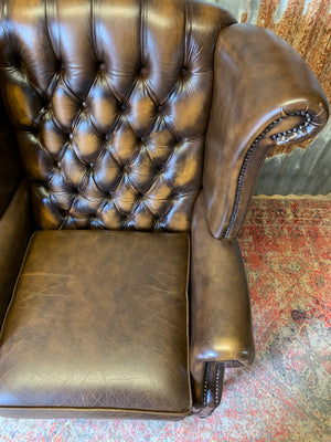 A brown wingback Chesterfield armchair with button back