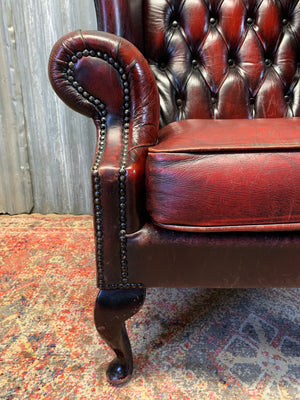 An oxblood wingback Queen Anne-style armchair