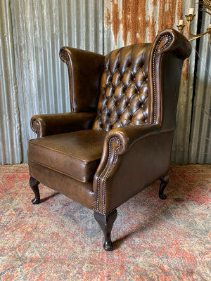 A brown wingback Chesterfield armchair with button back