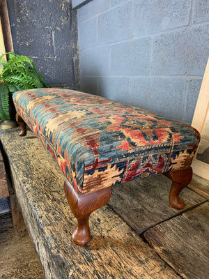 A large kilim-style footstool on cabriole legs