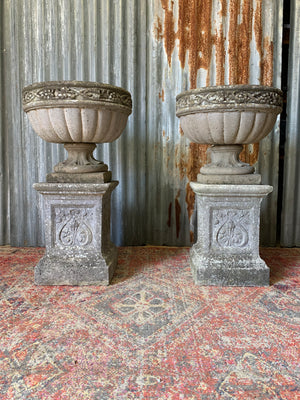 A pair of large cast stone classical urns on pedestals