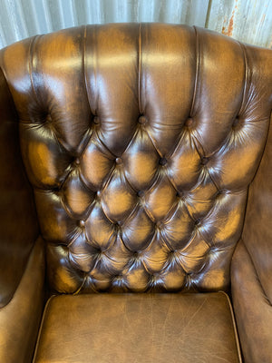 A brown wingback Chesterfield armchair with button back