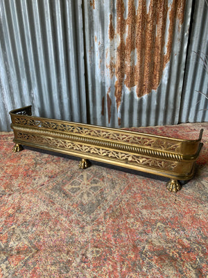 A large Victorian brass fender with lion paw feet