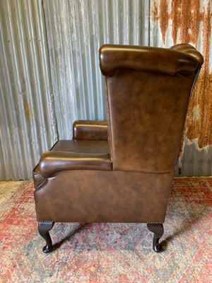 A brown wingback Chesterfield armchair with button back
