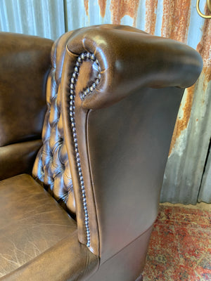 A brown wingback Chesterfield armchair with button back