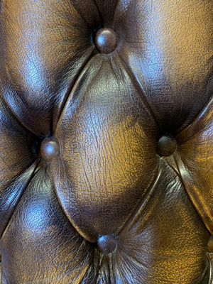 A brown wingback Chesterfield armchair with button back
