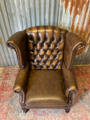 A brown wingback Chesterfield armchair with button back
