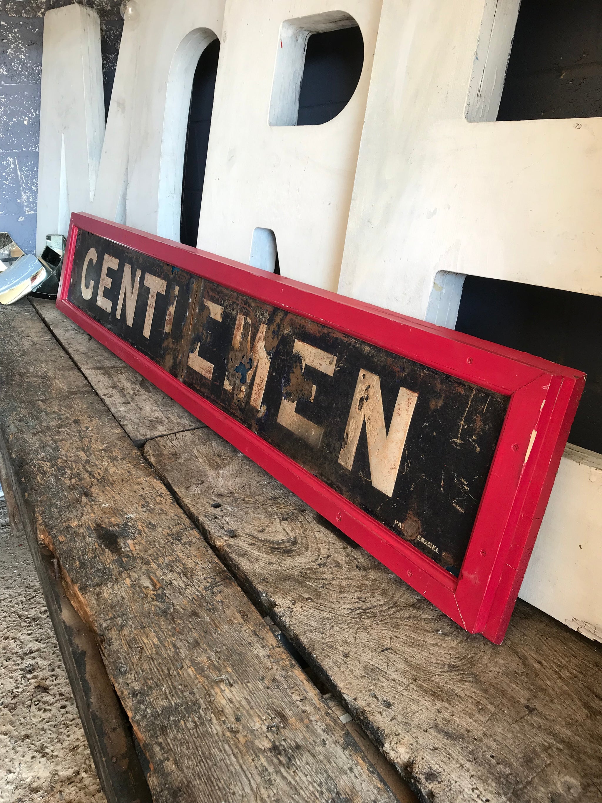 A large enamel GENTLEMEN sign in a wooden frame