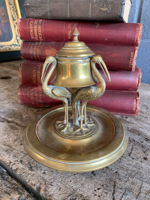 A brass inkwell supported by three storks
