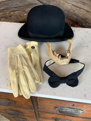 A vintage black bowler hat, bow tie and white gloves