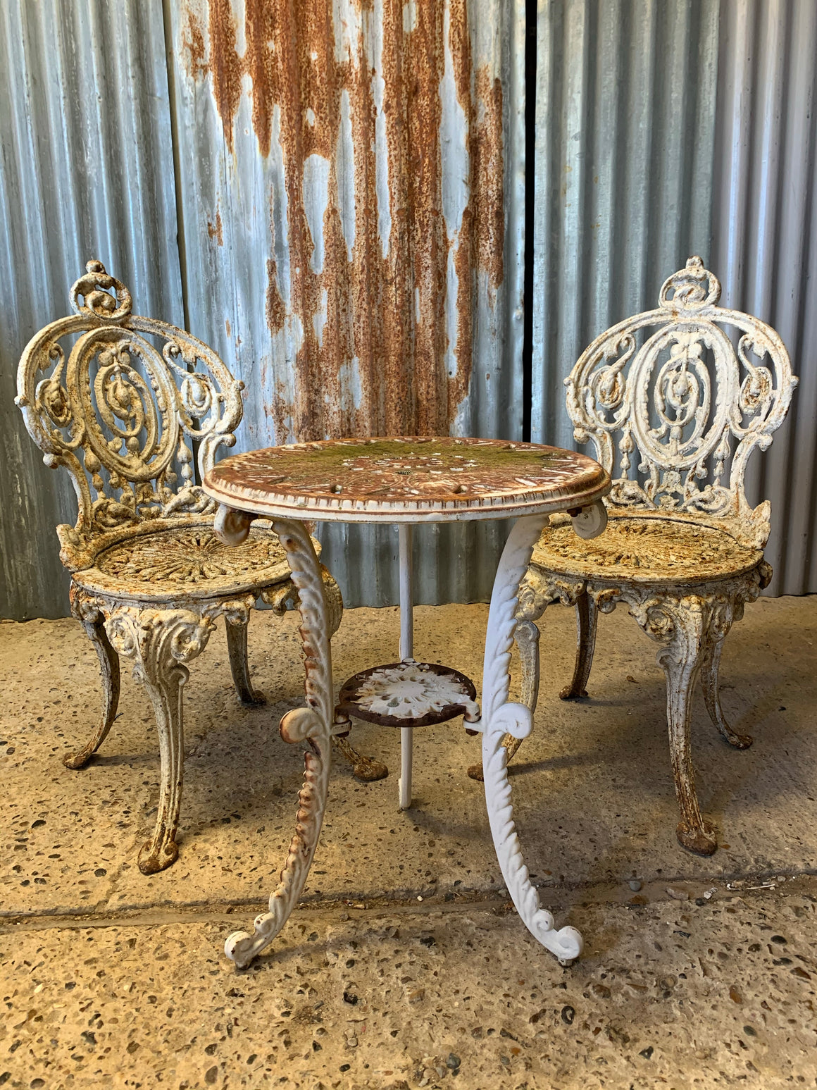 A pair of white cast iron Coalbrookdale chairs and complimentary bistro table