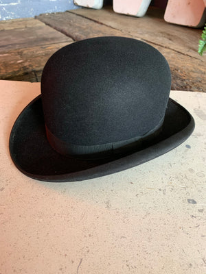 A vintage black bowler hat, bow tie and white gloves