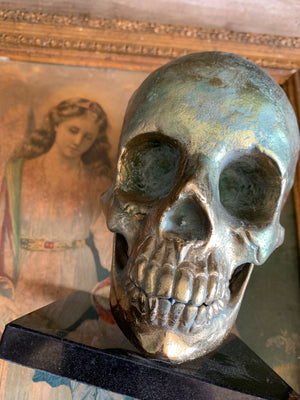 A brass human skull model mounted on a marble stand