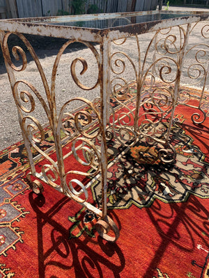 A weathered white wrought iron console table with glass top