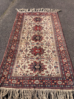 A cream ground Persian rectangular rug with long fringe- 260cm x 134cm