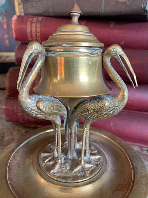A brass inkwell supported by three storks
