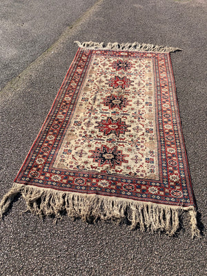 A cream ground Persian rectangular rug with long fringe- 260cm x 134cm