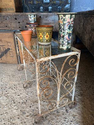 A weathered white wrought iron console table with glass top